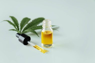 Cannabis sativa hemp leaf with container of CBD oil with dropper lid on white background. Legalized marihuana concept. clipart