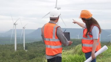 Erkek ve kadın mühendisler kırsal kesimdeki bir tepenin tepesinde ya da dağda rüzgar çiftliğinde çalışıyorlar. Yenilenebilir ve sürdürülebilir enerjinin gelecekteki üretimi için yenilikçi idealler.