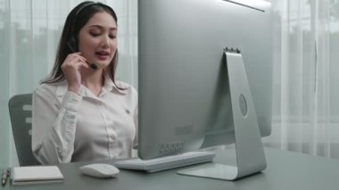 Masasında dizüstü bilgisayarla çalışan kulaklık ve mikrofon takan Asyalı müşteri destek operatörü. Hevesli kadın çalışanlar müşteri hizmetleri sunuyor, destekleyici çağrı merkezi temsilcisi müşterilere yardım ediyor.