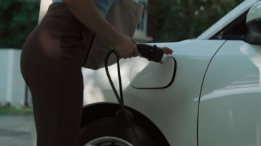 İlerici kadın evdeki elektrikli aracına şarj istasyonu fişi takıyor. EV otomobilleri çevreye yararlı temiz ve yeşil enerji kavramı sağlar.
