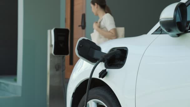 一个女人在他家拔掉了电动汽车充电器的插头 在进步的生活方式中使用电动汽车的概念有助于清洁和健康的环境 — 图库视频影像