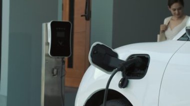 İlerici ebeveynler kızlarını okuldan alırken elektrikli araba ve yenilenebilir enerji kavramını kullandılar, evdeki EV otomobil için şarj istasyonu. Alternatif eko taşımacılığı.