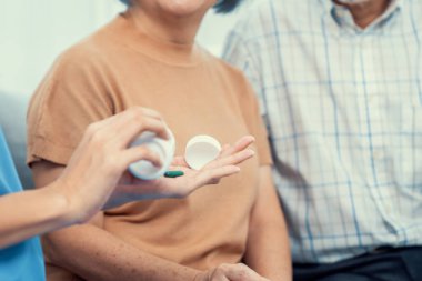 Contented senior woman sit along side with her husband, taking medicines while her caregiver advising her medication. Medication for seniors, nursing house, healthcare at home.