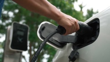 İlerici adam elektrikli aracına elektrik kablosu takıyor. Ev şarj istasyonundan EV arabası. Çevreyi korumak için temiz ve yenilenebilir enerji kullanan elektrikli bir araba. Çevre dostu otomobil.