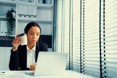 Competent female employee sits at her desk with a cup of coffee. Modern employee working with a drink, recreation during working hours, caffeine for people who are working
