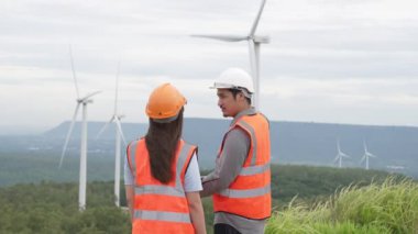 Erkek ve kadın mühendisler kırsal kesimdeki bir tepenin tepesinde ya da dağda rüzgar çiftliğinde çalışıyorlar. Yenilenebilir ve sürdürülebilir enerjinin gelecekteki üretimi için yenilikçi idealler.