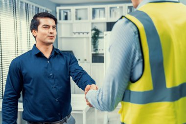 An engineer with a protective vest handshake with an investor in his office. Following a successful meeting, employee and employer form a partnership.