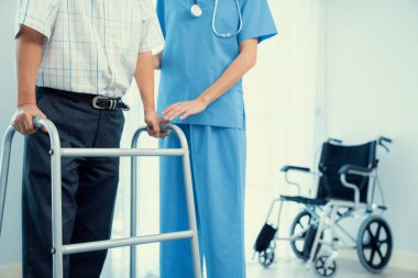 Physiotherapist assists her contented senior patient on folding walker. Recuperation for elderly, seniors care, nursing home.