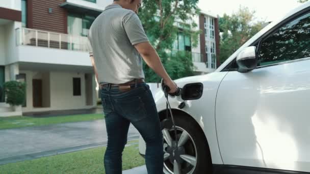 プログレッシブマンは 自宅の電気自動車のバッテリーに排出ガスのない電源コネクタを取り付けます 充電ステーションからEvカーバッテリーへのケーブルを介して電気自動車の充電 — ストック動画