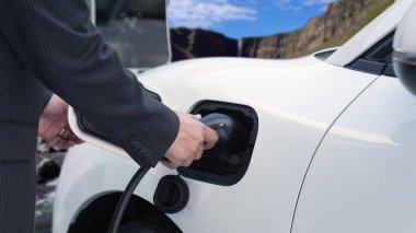 İlerici adam arka planda kırsal dağ olan şarj istasyonundan elektrik kablosu yerleştiriyor. Temiz ortam için elektro motor tarafından kullanılan EV otomobil