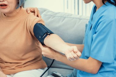 An elderly woman with a contented life having a blood pressure check by her caregiver at home with a smiley face.