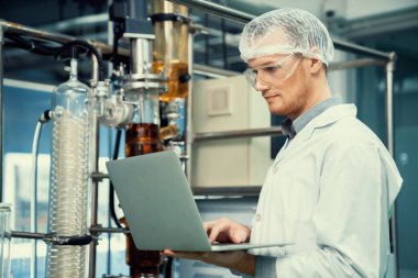 CBD yağ çıkarıcısının yanında dizüstü bilgisayarla çalışan eczacı bilim adamı ve tıbbi esrar ürünleri üretmek için kullanılan bilimsel bir makine.