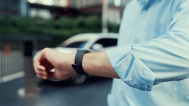 Takım elbiseli, hırslı bir işadamı elektrik kablosu ve yenilenebilir enerji enerjili bir elektrikli araçla şarj istasyonunda dururken elektrikli aracına yaslanıyor..