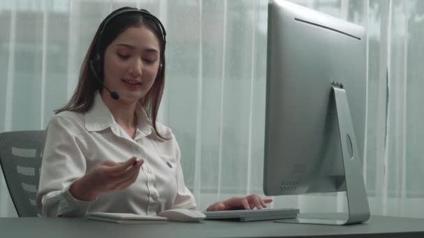 헤드폰 마이크를 아시아 업체가 노트북을 가지고 책상에서 일하고 있습니다 열정적 — 비디오