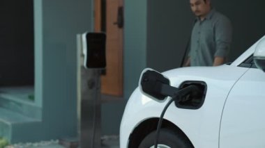 Adamın biri evinde elektrikli araç şarj aletinin fişini çekiyor. İlerici bir yaşam tarzında elektrikli araçların kullanımı, temiz ve sağlıklı bir çevreye katkıda bulunur..