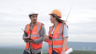 Erkek ve kadın mühendisler kırsal kesimdeki bir tepenin tepesinde ya da dağda rüzgar çiftliğinde çalışıyorlar. Yenilenebilir ve sürdürülebilir enerjinin gelecekteki üretimi için yenilikçi idealler.