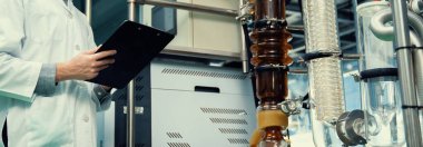 CBD yağ çıkarıcısından bilgi almak için pano ve kalem kullanan eczacı bilim adamı ve tıbbi esrar ürünleri üretmek için kullanılan bilimsel bir makine..