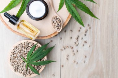 Kenevir ve kozmetik konseptinde CBD yağ şişeleri, krema kavanozu ve kenevir tohumları bulunur. Cilt ürünleri için yasallaştırılmış esrar.