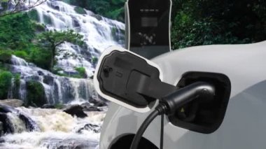 Elektrikli araba, doğal ortam, şelale ve akış arkaplanındaki şarj istasyonundan enerji yüklüyor. Yenilenebilir enerji kaynaklı EV otomobillerin enerji sürdürülebilirliği kavramı.