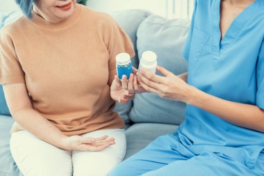 Caregiver advising contented senior woman on medication in the living room. Medication for seniors, nursing house, healthcare at home.