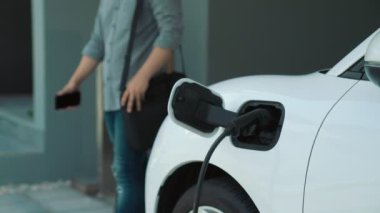 Adamın biri evinde elektrikli araç şarj aletinin fişini çekiyor. İlerici bir yaşam tarzında elektrikli araçların kullanımı, temiz ve sağlıklı bir çevreye katkıda bulunur..