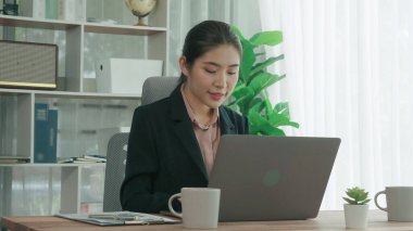 Ofiste çalışan ve dizüstü bilgisayar yazan hevesli bir iş kadını. Masasında oturmuş laptopla çalışan güzel bir ofis hanımı..