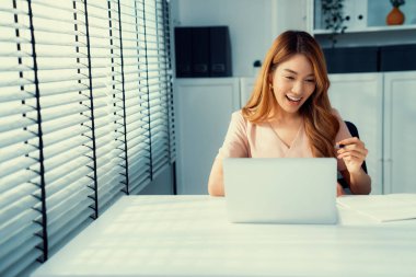 A young Asian female employee sitting at her desk in her office, sitting at desktop in workstation.