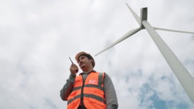 Gökyüzü arka planına sahip bir rüzgar türbini üzerinde çalışan mühendis. Yenilenebilir ve sürdürülebilir enerjinin gelecekteki üretimi için yenilikçi bir ideal. Rüzgar türbininden enerji üretimi.