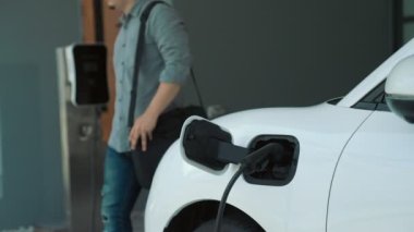 Adamın biri evinde elektrikli araç şarj aletinin fişini çekiyor. İlerici bir yaşam tarzında elektrikli araçların kullanımı, temiz ve sağlıklı bir çevreye katkıda bulunur..