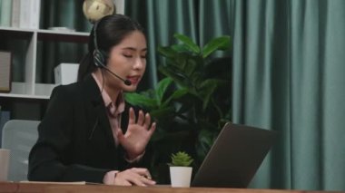 Kulaklık ve mikrofon takan iş kadını masasında çalışıyor ve dizüstü bilgisayar kullanıyor. Uzaktan kumandalı online toplantı için dizüstü bilgisayar kullanan hevesli kadın çalışanlar, ofiste iş videosu konferansı.