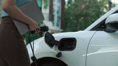 İlerici kadın evdeki elektrikli aracına şarj istasyonu fişi takıyor. EV otomobilleri çevreye yararlı temiz ve yeşil enerji kavramı sağlar.
