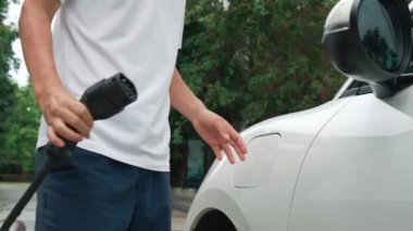 İlerici adam elektrikli aracına elektrik kablosu takıyor. Ev şarj istasyonundan EV arabası. Çevreyi korumak için temiz ve yenilenebilir enerji kullanan elektrikli bir araba. Çevre dostu otomobil.