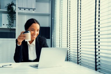 Competent female employee sits at her desk with a cup of coffee. Modern employee working with a drink, recreation during working hours, caffeine for people who are working