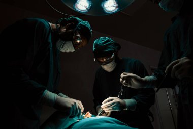 Steril ameliyathanedeki hastaya ameliyat yapan cerrahi ekip. Bir lambanın yaktığı ameliyathanede, profesyonel ve kendinden emin bir cerrahi ekip bilinçsiz bir hastaya tıbbi bakım sağlar..