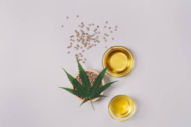 CBD oil, THC tinture in glass bowl and bottle with dropper lid and hemp leaf on empty background with a pile of dry hemp seeds surrounded in minimalism. Legalized marijuana concept. clipart