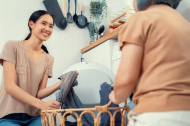 Daughter and mother working together to complete their household chores near the washing machine in a happy and contented manner. Mother and daughter doing the usual tasks in the house.