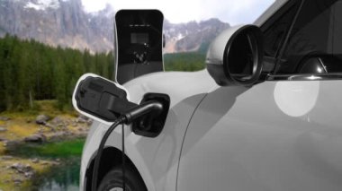 Elektro jeneratör sürücüsüyle enerji sürdürülebilir araba gücü, şarj istasyonunda şarj edilen batarya, ilerici seyahat konsepti için dağ zeminine sahip. Temiz ortamın sembolü olarak doğadaki EV otomobil.