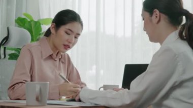 Ofis çalışma alanında birlikte çalışan iki genç hevesli iş kadını. Genç meslektaşlar tartışırken ve dizüstü bilgisayar kullanırken. Modern ofis çalışanları masada birlikte oturuyorlar..