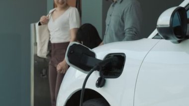 İlerici ebeveynler kızlarını okuldan alırken elektrikli araba ve yenilenebilir enerji kavramını kullandılar, evdeki EV otomobil için şarj istasyonu. Alternatif eko taşımacılığı.