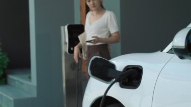 Evinde şarj edilen elektrikli bir araçla işten yeni dönen modern bir kadının ilerici yaşam tarzı. Elektrikli araç, sürdürülebilir temiz enerjiyle çalışıyor..