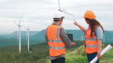 Erkek ve kadın mühendisler kırsal kesimdeki bir tepenin tepesinde ya da dağda rüzgar çiftliğinde çalışıyorlar. Yenilenebilir ve sürdürülebilir enerjinin gelecekteki üretimi için yenilikçi idealler.