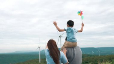 İlerici mutlu aile kavramı rüzgâr türbini çiftliğinde eğleniyor. Rüzgar türbini jeneratörüyle gelen elektrik jeneratörü kırsal bölgede tepe ve ufukta dağ var..
