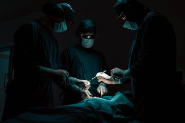 Steril ameliyathanedeki hastaya ameliyat yapan cerrahi ekip. Bir lambanın yaktığı ameliyathanede, profesyonel ve kendinden emin bir cerrahi ekip bilinçsiz bir hastaya tıbbi bakım sağlar..