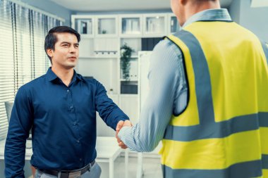 An engineer with a protective vest handshake with an investor in his office. Following a successful meeting, employee and employer form a partnership.