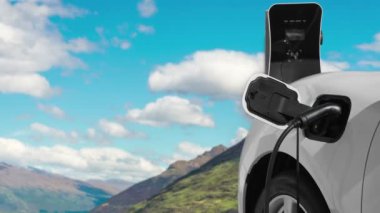 Temiz çevre için temiz enerjinin yol açtığı ilerici elektrikli araba kavramının arka planı olarak dağın tepesinde bulutun zaman kavramının yer aldığı doğal manzara. EV araba şarj istasyonunda şarj oluyor..