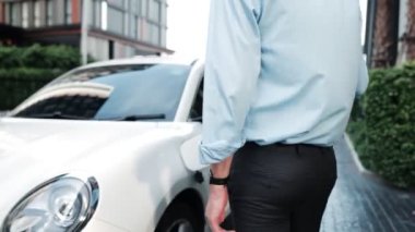 İlerici işadamı, şehir merkezinde dolaşmadan önce şarj cihazından elektrikli arabasına şarj prizi takıyor. Çevre dostu şarj edilebilir araba, sürdürülebilir ve temiz enerjiyle çalışıyor..