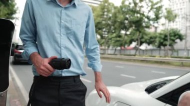 İlerici işadamı ve iş kadını, şehir merkezinde dolaşmadan önce şarj cihazını şarj istasyonundan elektrikli arabaya takıyor. Çevre dostu şarj edilebilir araba temiz enerjiyle çalışıyor..