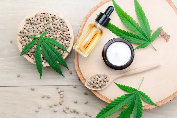 stock image Cannabis and cosmetic concept features with set of CBD oil bottles, cream jar, and wooden bowl of hemp seeds. Legalized cannabis for skincare products.