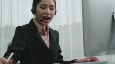 Masasında dizüstü bilgisayarla çalışan kulaklık ve mikrofon takan Asyalı müşteri destek operatörü. Hevesli kadın çalışanlar müşteri hizmetleri sunuyor, destekleyici çağrı merkezi temsilcisi müşterilere yardım ediyor.