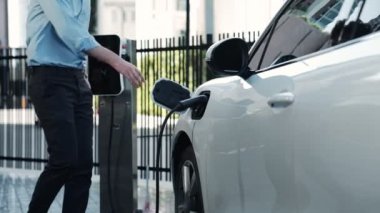 İlerici işadamı, şehir merkezinde dolaşmadan önce şarj cihazından elektrikli arabasına şarj prizi takıyor. Çevre dostu şarj edilebilir araba, sürdürülebilir ve temiz enerjiyle çalışıyor..